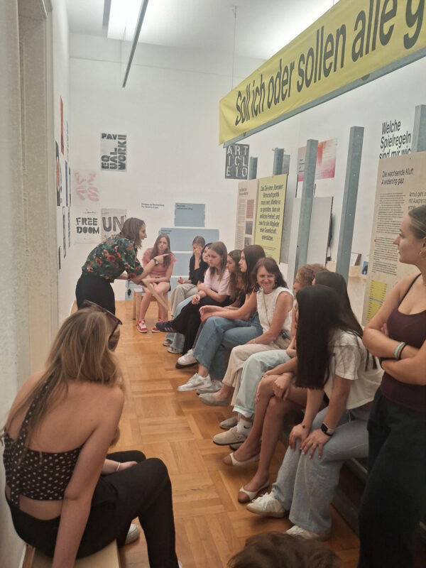 Ausstellung: Eine Frau erklärt einer Gruppe junger Leute eine Ausstellung in Wien.