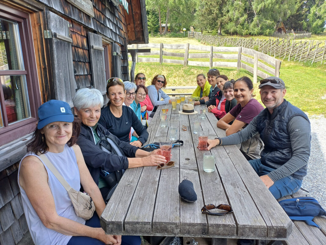 Gruppe von Menschen sitzt an einem Holztisch vor einer Hütte in den Bergen