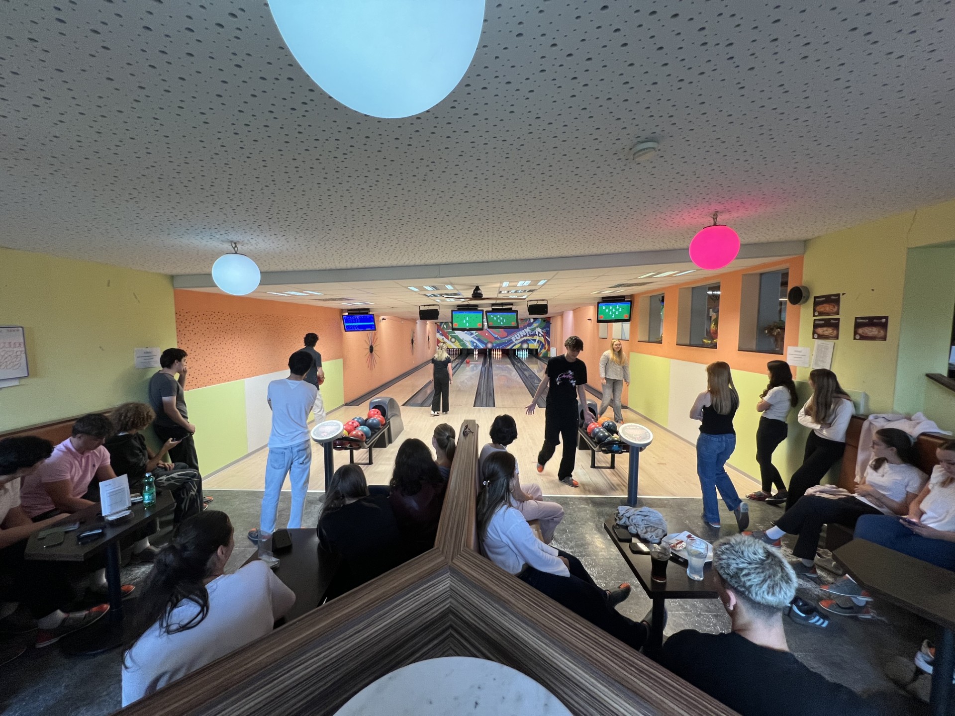 Jugendliche beim Bowling in einer Halle mit bunten Wänden und Deckenlampen