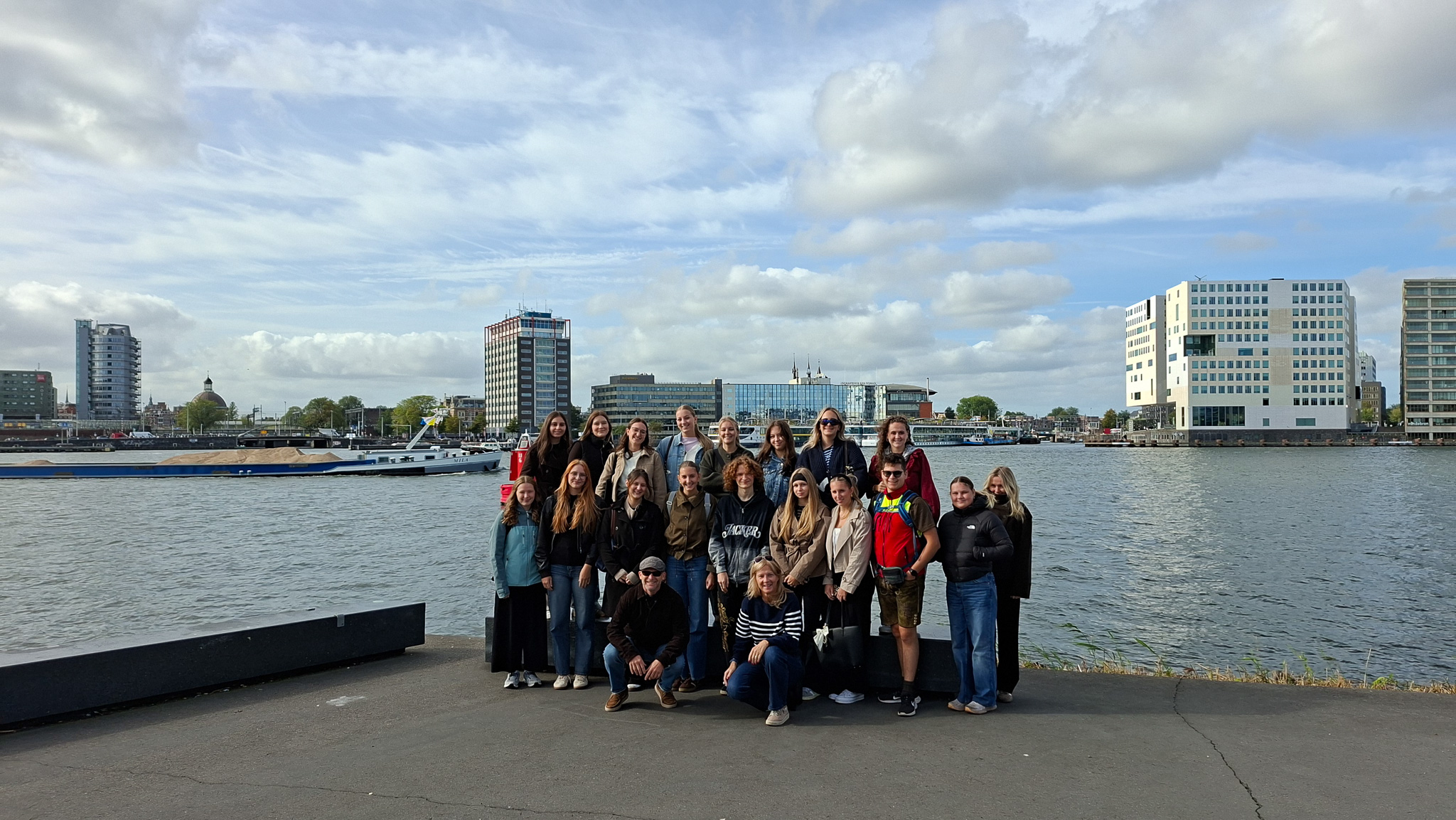 Gruppe von jungen Leuten steht am Wasser vor moderner Architektur in Amsterdam